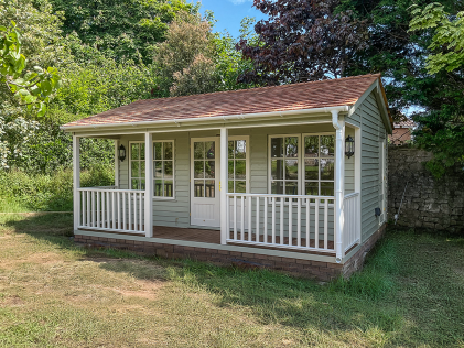 Grey Pavilion Garden Room featuring a white picket fence-lined veranda with roof overhang and traditional weatherboard cladding